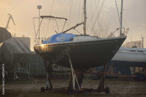 Winterized sloop rigged yacht standing on land, close-up. Waiting for the new sailing season. Yacht club (marina) at sunset. Soft evening light. Nautical vessel, service, transportation photo