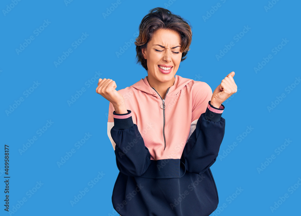 Young beautiful woman wearing sportswear excited for success with arms raised and eyes closed celebrating victory smiling. winner concept. Young beautiful woman wearing sportswear excited for success with arms raised and eyes closed celebrating victory smiling. winner concept.