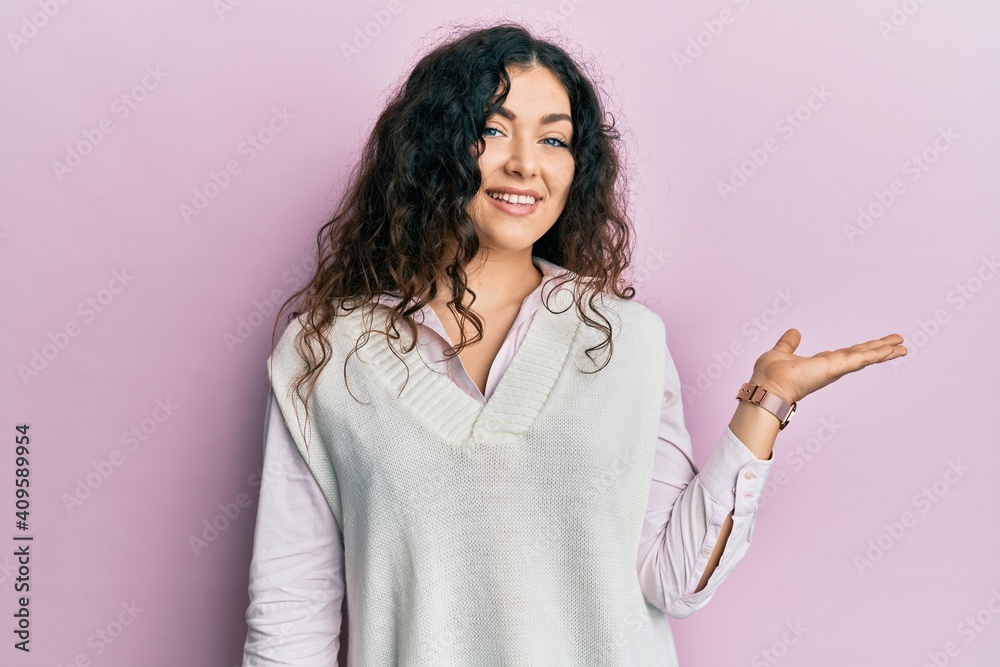 Young brunette woman with curly hair wearing casual clothes smiling cheerful presenting and pointing with palm of hand looking at the camera. Young brunette woman with curly hair wearing casual clothes smiling cheerful presenting and pointing with palm of hand looking at the camera.