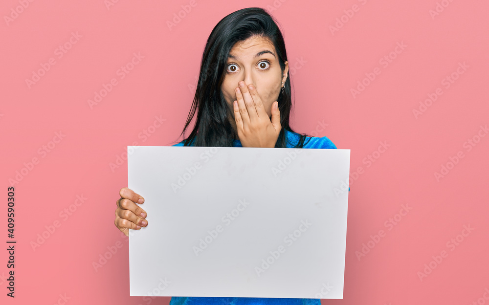 Young hispanic woman holding blank empty banner covering mouth with hand, shocked and afraid for mistake. surprised expression - obrazy, fototapety, plakaty 