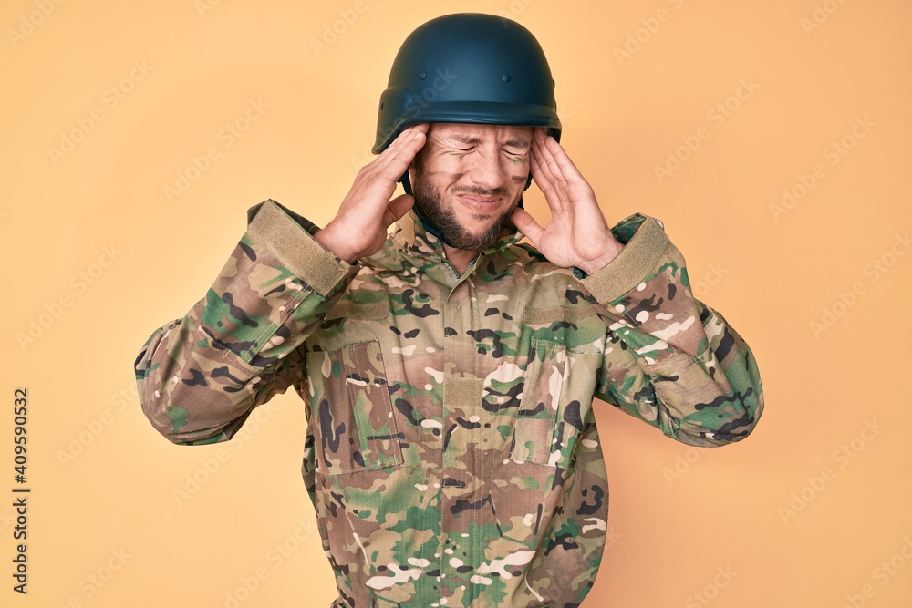Young caucasian man wearing camouflage army uniform with hand on head, headache because stress. suffering migraine.