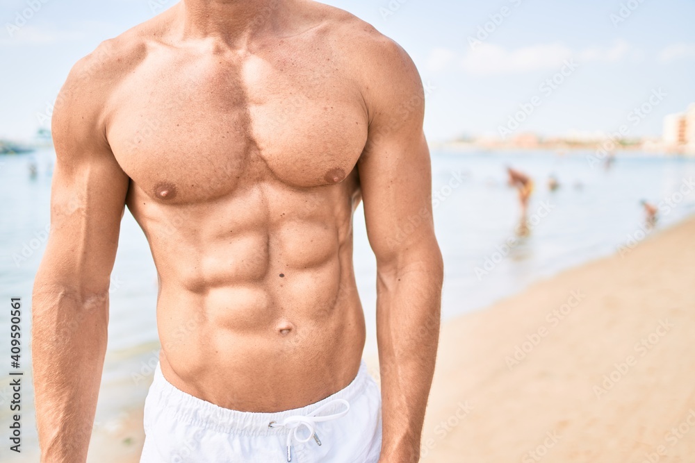 Obraz premium Handsome fitness caucasian man at the beach on a sunny day showing muscular fitness body