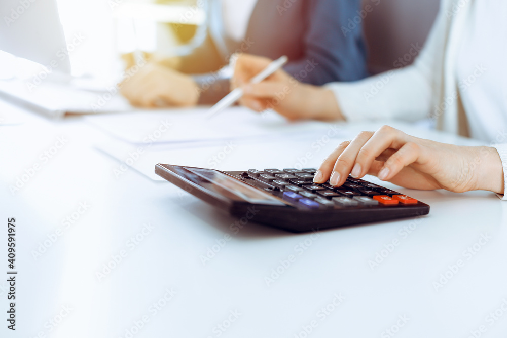 Accountant checking financial statement or counting by calculator income for tax form, hands closeup. Business woman sitting and working with colleague at the desk in office. Tax and Audit concept - obrazy, fototapety, plakaty 