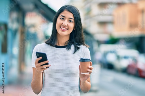 Young hispanic woman smiling happy using smartphone and drinking take away coffee at the city.
