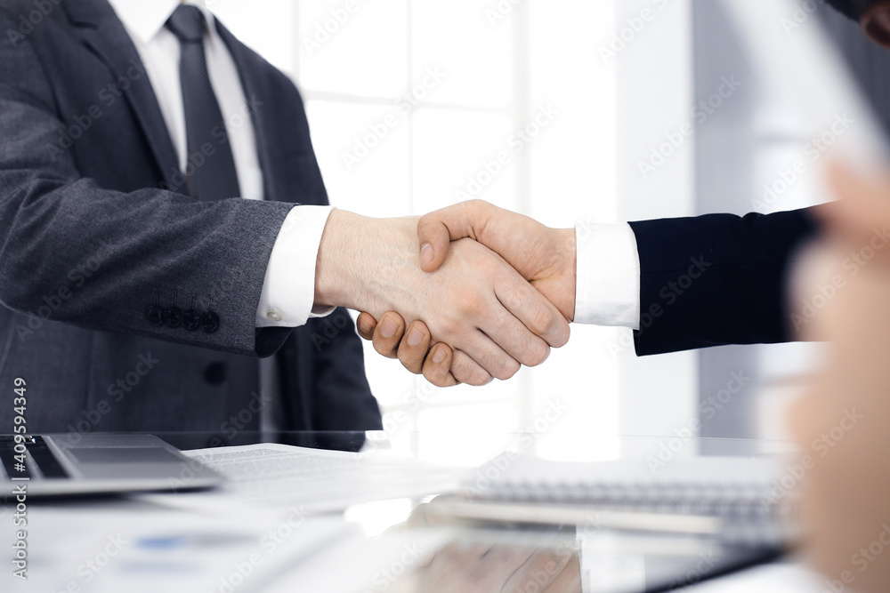 Unknown diverse business people are shaking hands finishing up meeting at the desk in office, close-up. Handshake concept