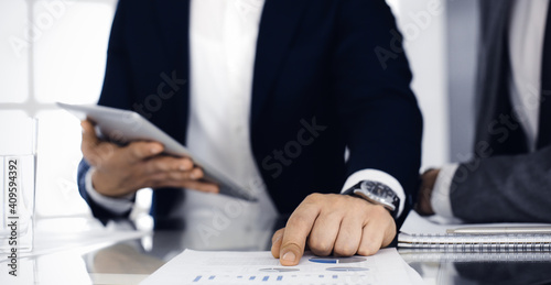 Business people using tablet computer while working together in modern office. Unknown businessman sitting at the desk with his colleague or partner. Teamwork and partnership concept