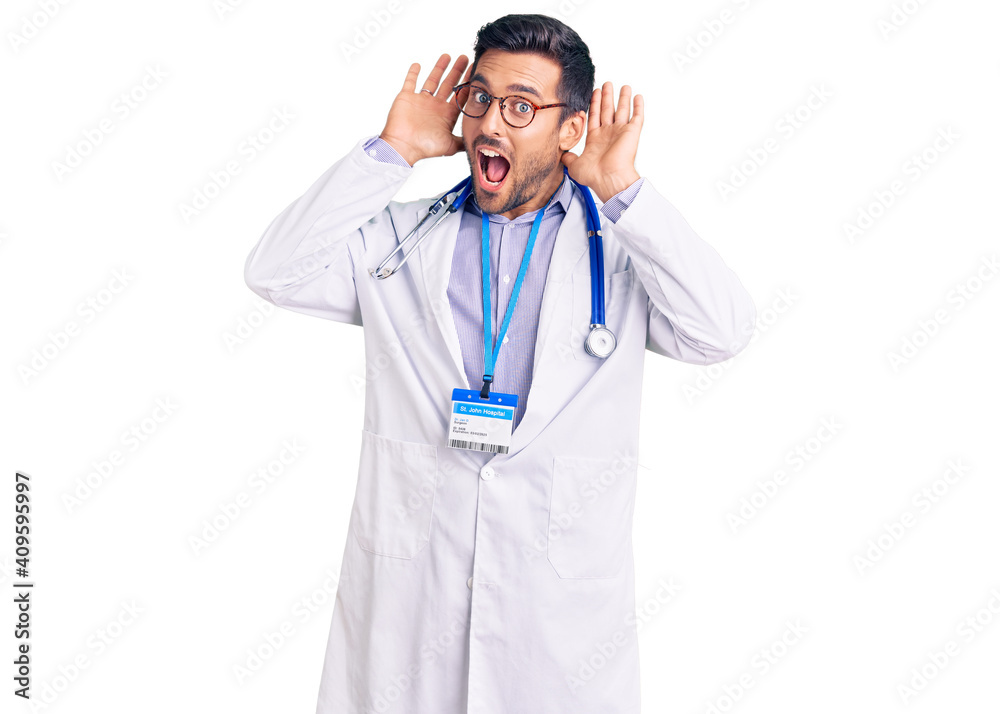 Young hispanic man wearing doctor uniform and stethoscope smiling cheerful playing peek a boo with hands showing face. surprised and exited Young hispanic man wearing doctor uniform and stethoscope smiling cheerful playing peek a boo with hands showing face. surprised and exited
