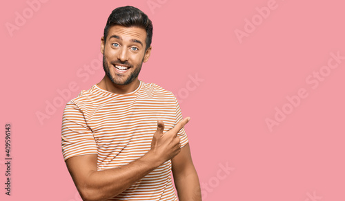 Handsome hispanic man wearing casual clothes cheerful with a smile on face pointing with hand and finger up to the side with happy and natural expression