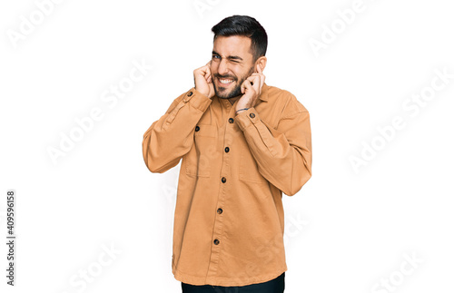 Young hispanic man wearing casual clothes covering ears with fingers with annoyed expression for the noise of loud music. deaf concept. © Krakenimages.com