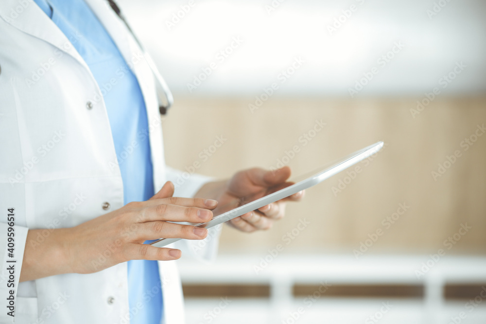Unknown woman-doctor standing in clinic and using tablet pc, close-up. Data in medicine and healthcare