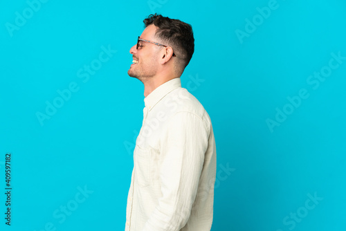 Young caucasian handsome man isolated on blue background laughing in lateral position © luismolinero