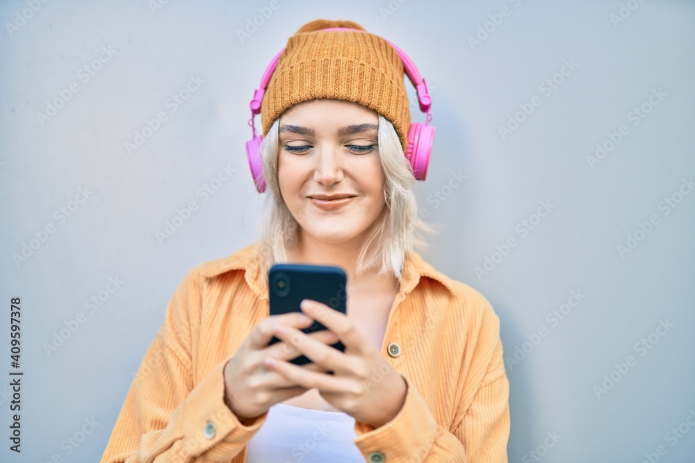 Young blonde girl smiling happy using smartphone and headphones at the city. Young blonde girl smiling happy using smartphone and headphones at the city.