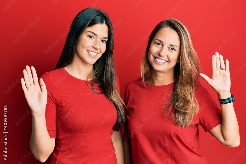 Hispanic family of mother and daughter wearing casual clothes over red background waiving saying hello happy and smiling, friendly welcome gesture Hispanic family of mother and daughter wearing casual clothes over red background waiving saying hello happy and smiling, friendly welcome gesture