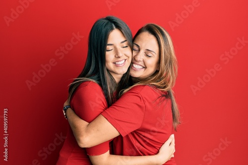 Obraz na płótnie Hispanic family of mother and daughter wearing casual clothes over red background hugging oneself happy and positive, smiling confident