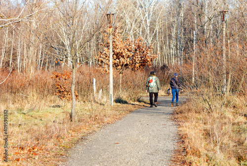 People walk along the path of the old park in the dry winter season on a bright sunny day.