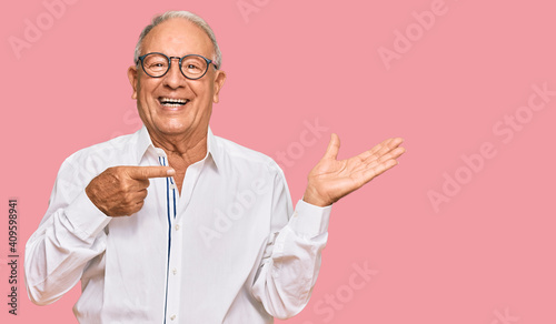 Senior caucasian man wearing business shirt and glasses amazed and smiling to the camera while presenting with hand and pointing with finger.