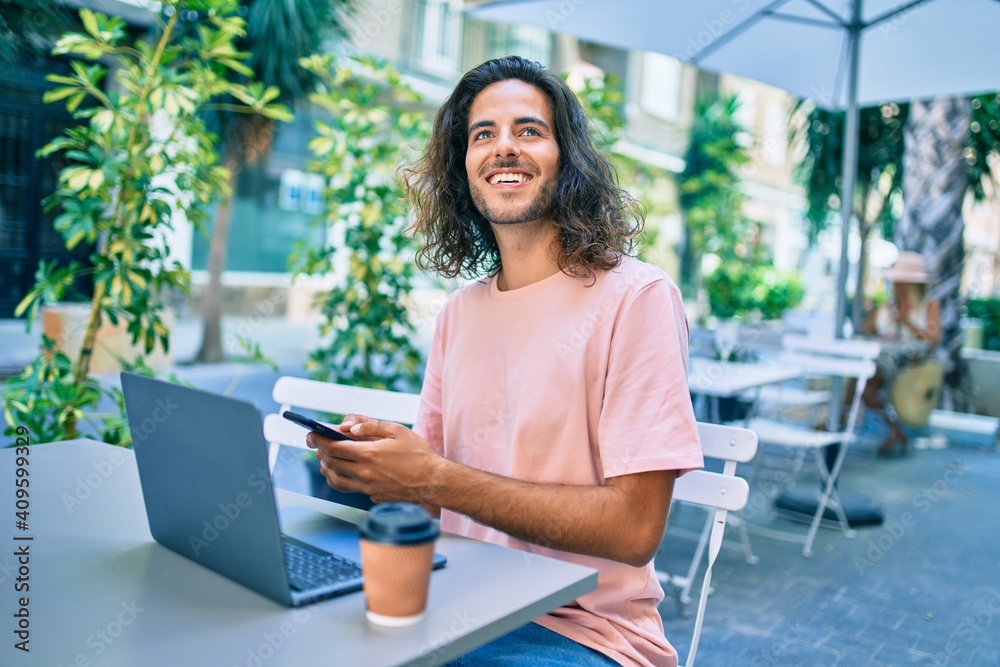 Young hispanic man smiling happy working using laptop and smartphone at terrace of coffee shop. Young hispanic man smiling happy working using laptop and smartphone at terrace of coffee shop.