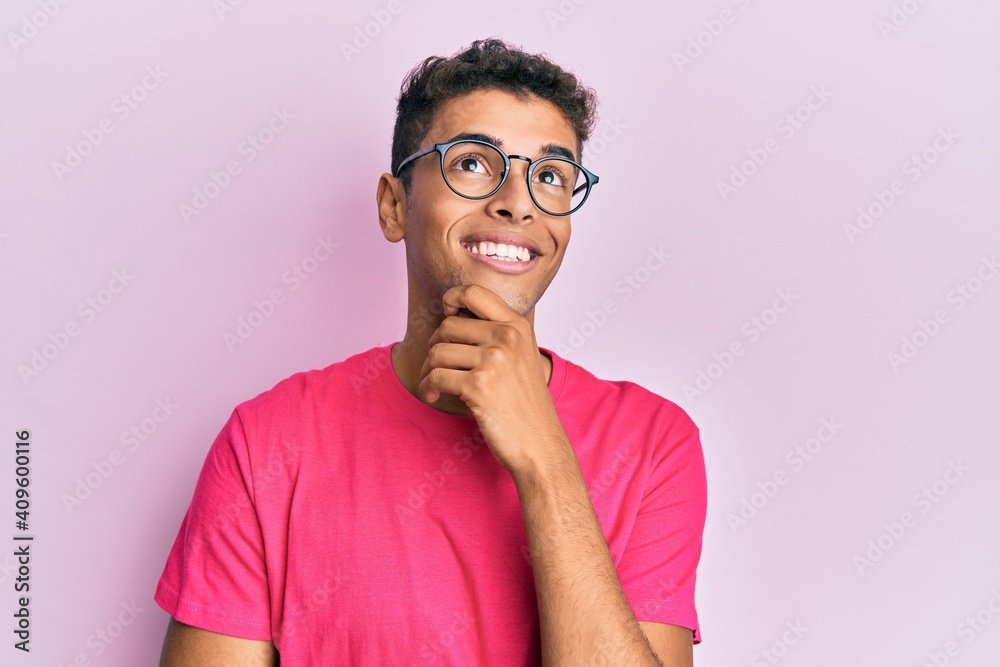 Young handsome african american man wearing glasses over pink background with hand on chin thinking about question, pensive expression. smiling with thoughtful face. doubt concept. Young handsome african american man wearing glasses over pink background with hand on chin thinking about question, pensive expression. smiling with thoughtful face. doubt concept.