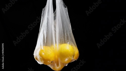 Ripe yellow lemons lie in a transparent plastic bag on a black background, close up