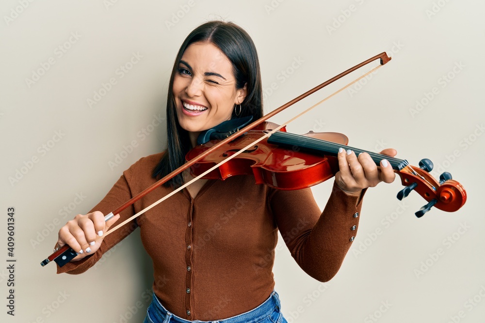 Young brunette woman playing violin winking looking at the camera with sexy expression, cheerful and happy face. Young brunette woman playing violin winking looking at the camera with sexy expression, cheerful and happy face.