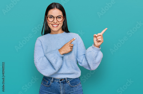 Young hispanic woman wearing casual clothes and glasses smiling and looking at the camera pointing with two hands and fingers to the side. photo