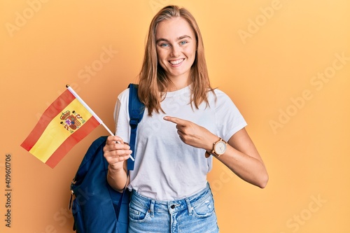 Beautiful blonde woman exchange student holding spanish flag smiling happy pointing with hand and finger photo