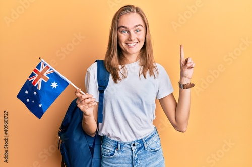 Beautiful blonde woman exchange student holding australia flag smiling with an idea or question pointing finger with happy face  number one