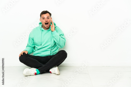 Young handsome caucasian man sitting on the floor with surprise and shocked facial expression