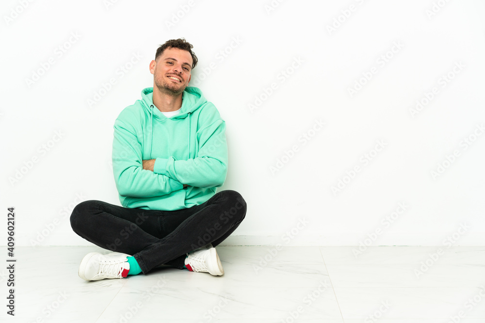 Young handsome caucasian man sitting on the floor with arms crossed and looking forward