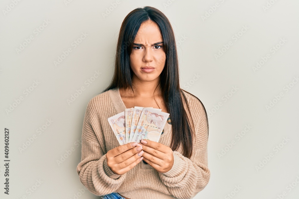 Young beautiful hispanic girl holding 10 united kingdom pounds banknotes skeptic and nervous, frowning upset because of problem. negative person. Young beautiful hispanic girl holding 10 united kingdom pounds banknotes skeptic and nervous, frowning upset because of problem. negative person.