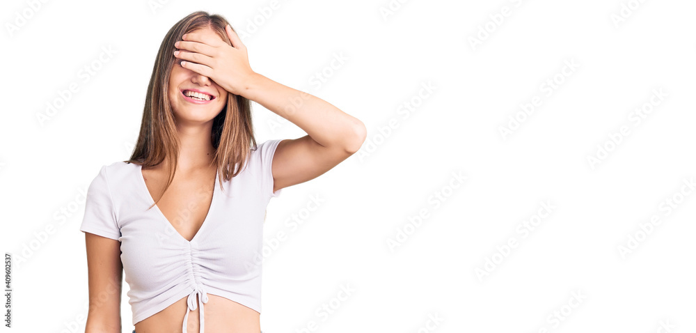 Young beautiful blonde woman wearing casual white tshirt smiling and laughing with hand on face covering eyes for surprise. blind concept. Young beautiful blonde woman wearing casual white tshirt smiling and laughing with hand on face covering eyes for surprise. blind concept.
