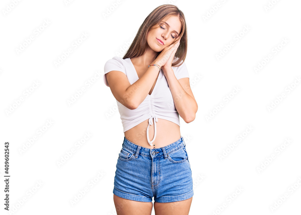 Young beautiful blonde woman wearing casual white tshirt sleeping tired dreaming and posing with hands together while smiling with closed eyes. Young beautiful blonde woman wearing casual white tshirt sleeping tired dreaming and posing with hands together while smiling with closed eyes.