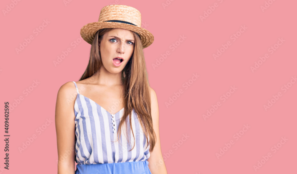 Young beautiful blonde woman wearing summer hat in shock face, looking skeptical and sarcastic, surprised with open mouth Young beautiful blonde woman wearing summer hat in shock face, looking skeptical and sarcastic, surprised with open mouth