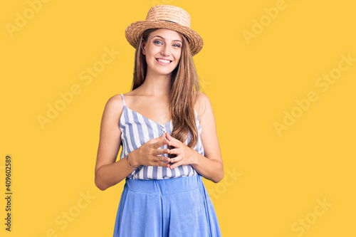 Young beautiful blonde woman wearing summer hat hands together and fingers crossed smiling relaxed and cheerful. success and optimistic
