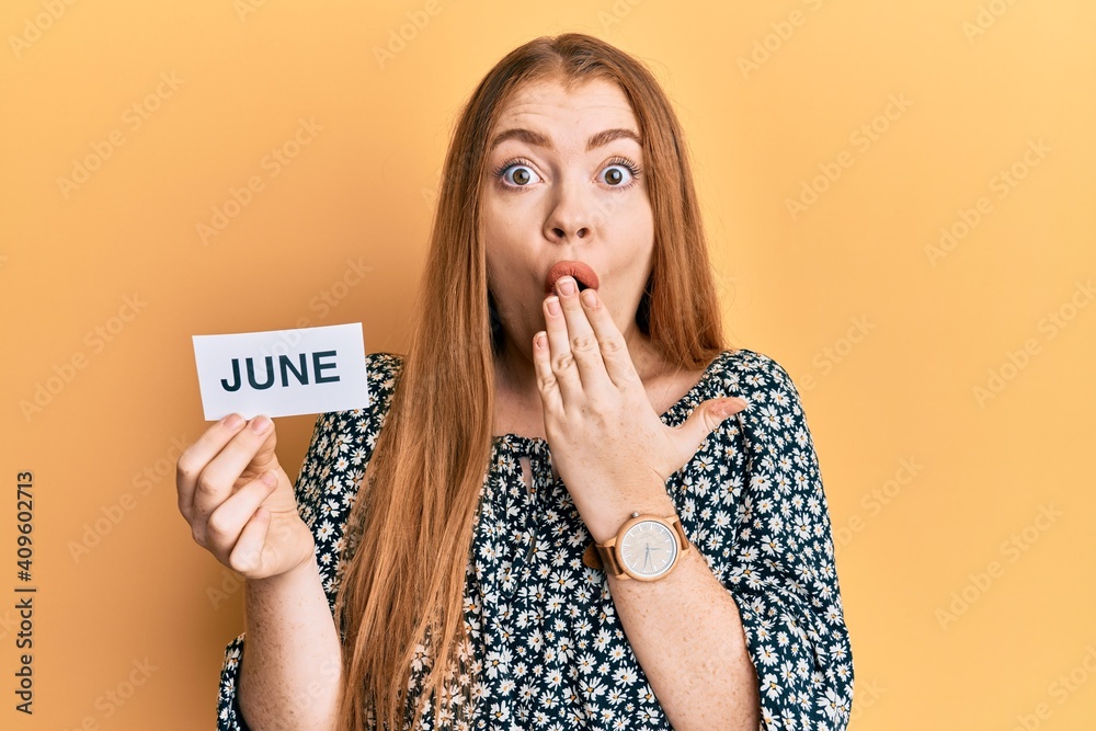 Young beautiful redhead woman holding june word on paper covering mouth with hand, shocked and afraid for mistake. surprised expression - obrazy, fototapety, plakaty 