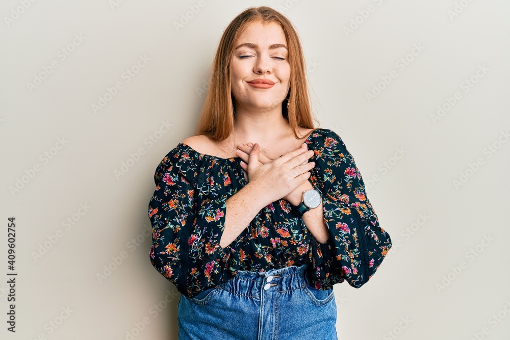Young beautiful redhead woman wearing casual floral clothes smiling with hands on chest, eyes closed with grateful gesture on face. health concept. Young beautiful redhead woman wearing casual floral clothes smiling with hands on chest, eyes closed with grateful gesture on face. health concept.