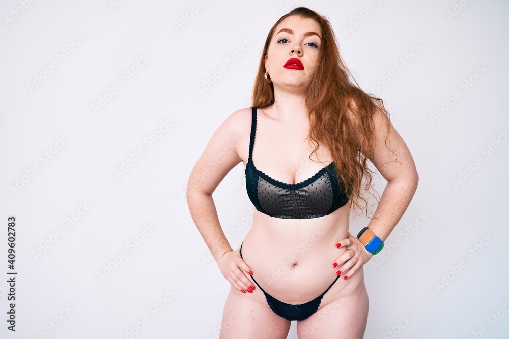 Young plus size redhead woman wearing sexy lingerie standing over isolated white background Young plus size redhead woman wearing sexy lingerie standing over isolated white background