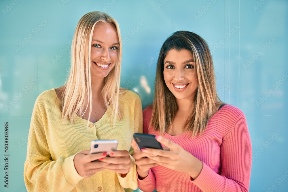 Fototapeta premium Two beautiful and young girl friends together having fun at the city using smartphone