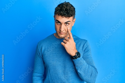 Hispanic young man wearing casual winter sweater pointing to the eye watching you gesture, suspicious expression © Krakenimages.com