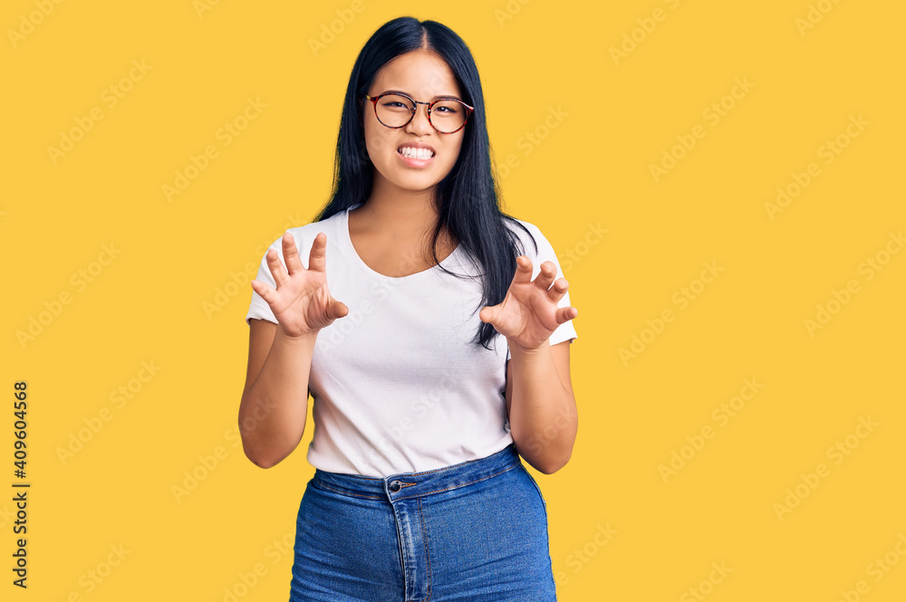Young beautiful asian girl wearing casual clothes and glasses smiling funny doing claw gesture as cat, aggressive and sexy expression Young beautiful asian girl wearing casual clothes and glasses smiling funny doing claw gesture as cat, aggressive and sexy expression