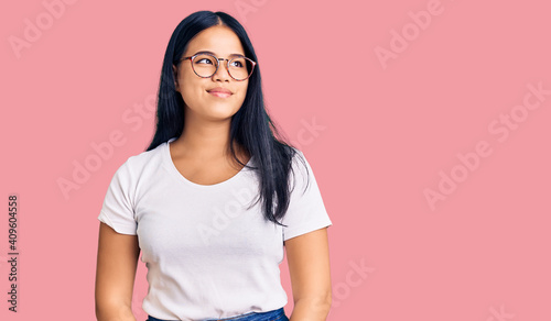 Young beautiful asian girl wearing casual clothes and glasses smiling looking to the side and staring away thinking.