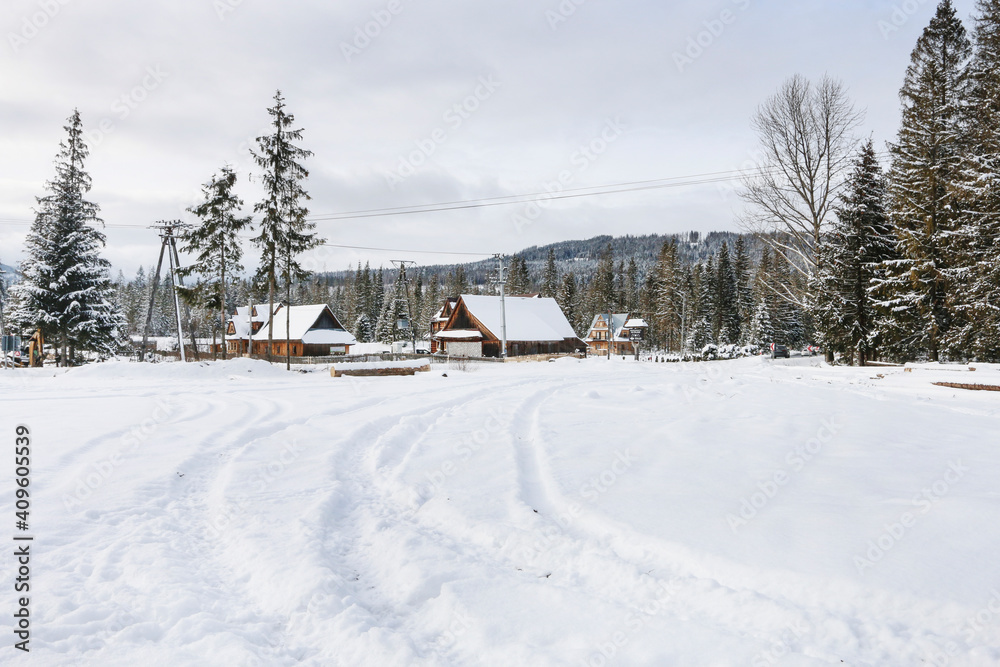 ZAKOPANE, POLAND - JANUARY 28, 2021: A settlement of small wooden houses near the forest, in the mountains. Winter landscape