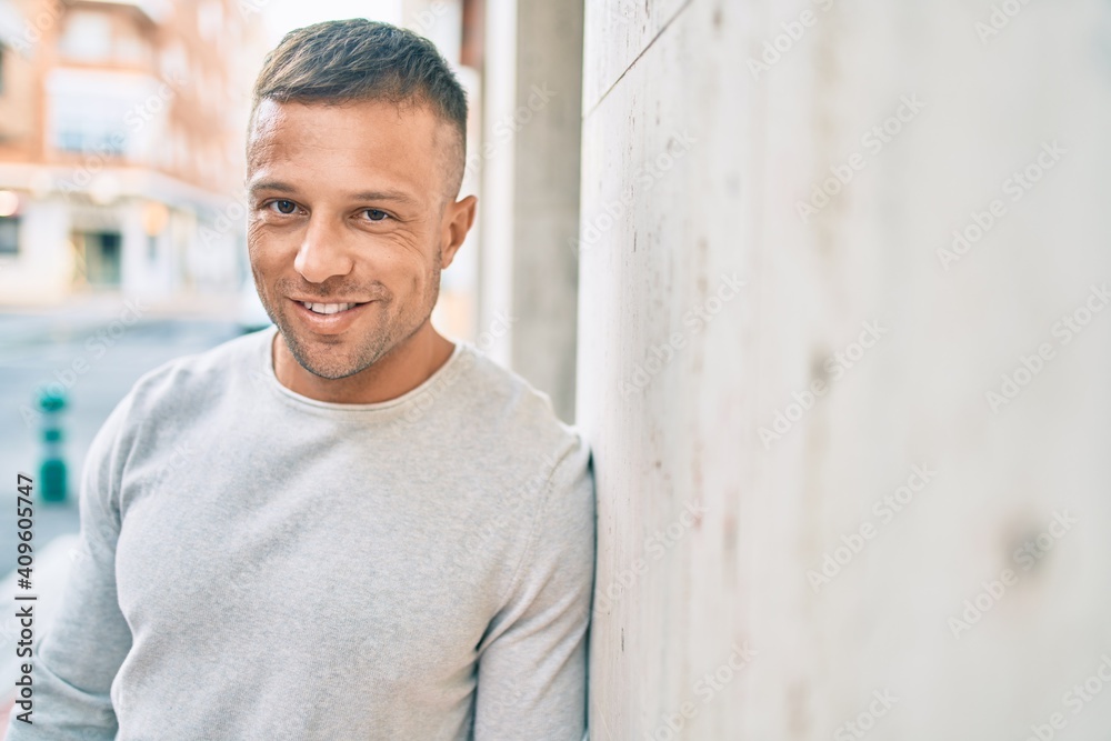 Obraz premium Young caucasian man smiling happy leaning on the wall at the city.
