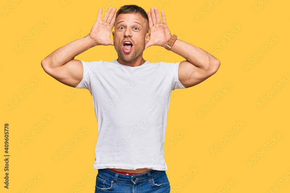 Handsome muscle man wearing casual white tshirt smiling cheerful playing peek a boo with hands showing face. surprised and exited Handsome muscle man wearing casual white tshirt smiling cheerful playing peek a boo with hands showing face. surprised and exited