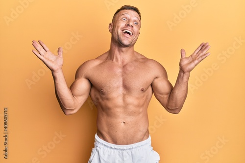 Handsome muscle man standing shirtless celebrating victory with happy smile and winner expression with raised hands