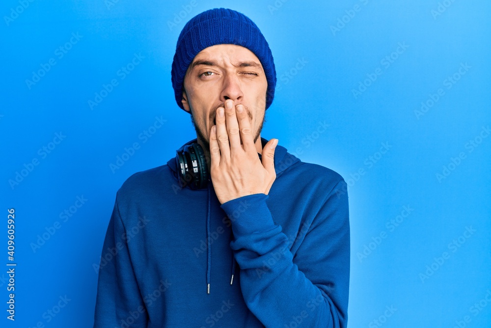 Hispanic young man wearing sweatshirt and headphones bored yawning tired covering mouth with hand. restless and sleepiness. Hispanic young man wearing sweatshirt and headphones bored yawning tired covering mouth with hand. restless and sleepiness.