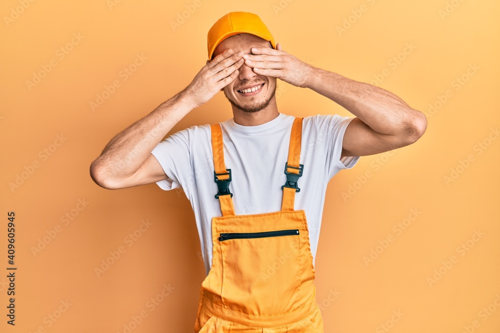 Hispanic young man wearing handyman uniform covering eyes with hands smiling cheerful and funny. blind concept.