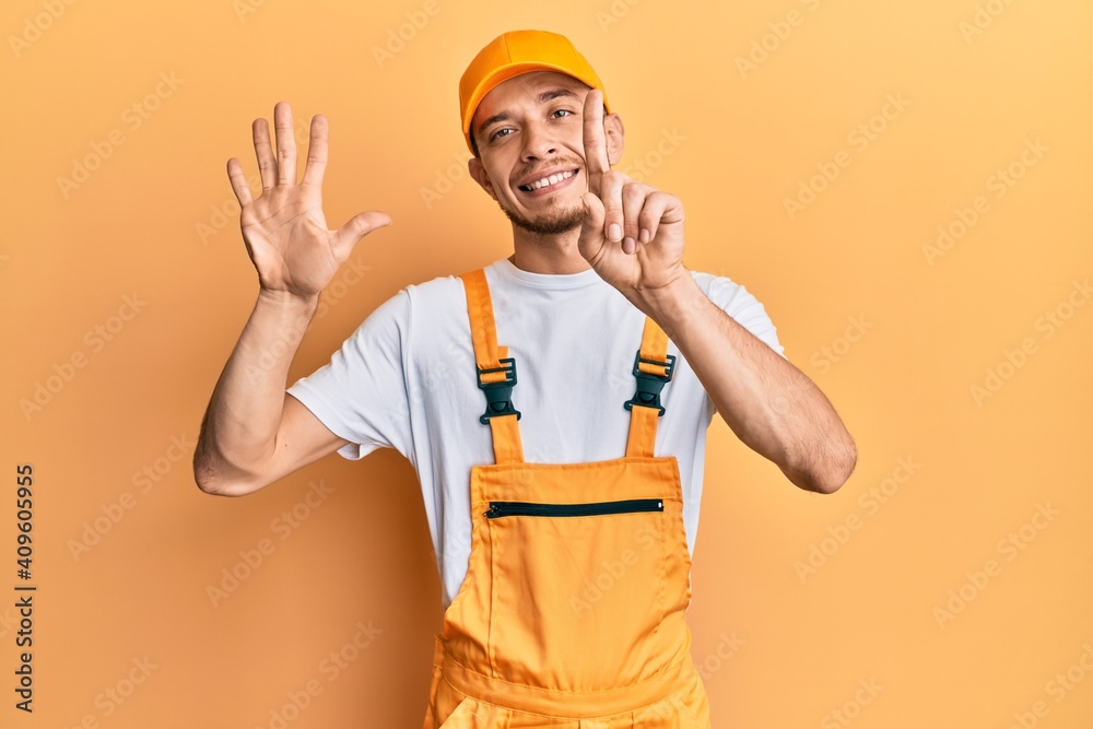 Hispanic young man wearing handyman uniform showing and pointing up with fingers number six while smiling confident and happy.