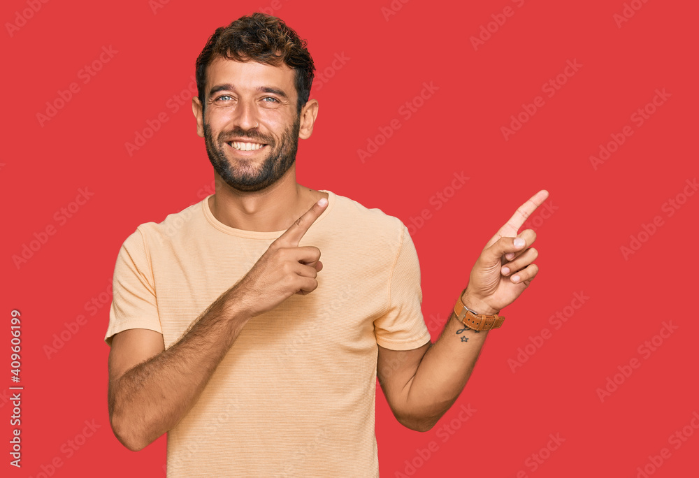 Handsome young man with beard wearing casual tshirt smiling and looking at the camera pointing with two hands and fingers to the side. Handsome young man with beard wearing casual tshirt smiling and looking at the camera pointing with two hands and fingers to the side.