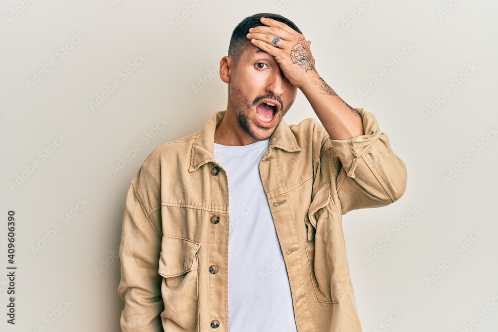 Handsome man with tattoos wearing casual brown denim jacket surprised with hand on head for mistake, remember error. forgot, bad memory concept. Handsome man with tattoos wearing casual brown denim jacket surprised with hand on head for mistake, remember error. forgot, bad memory concept.